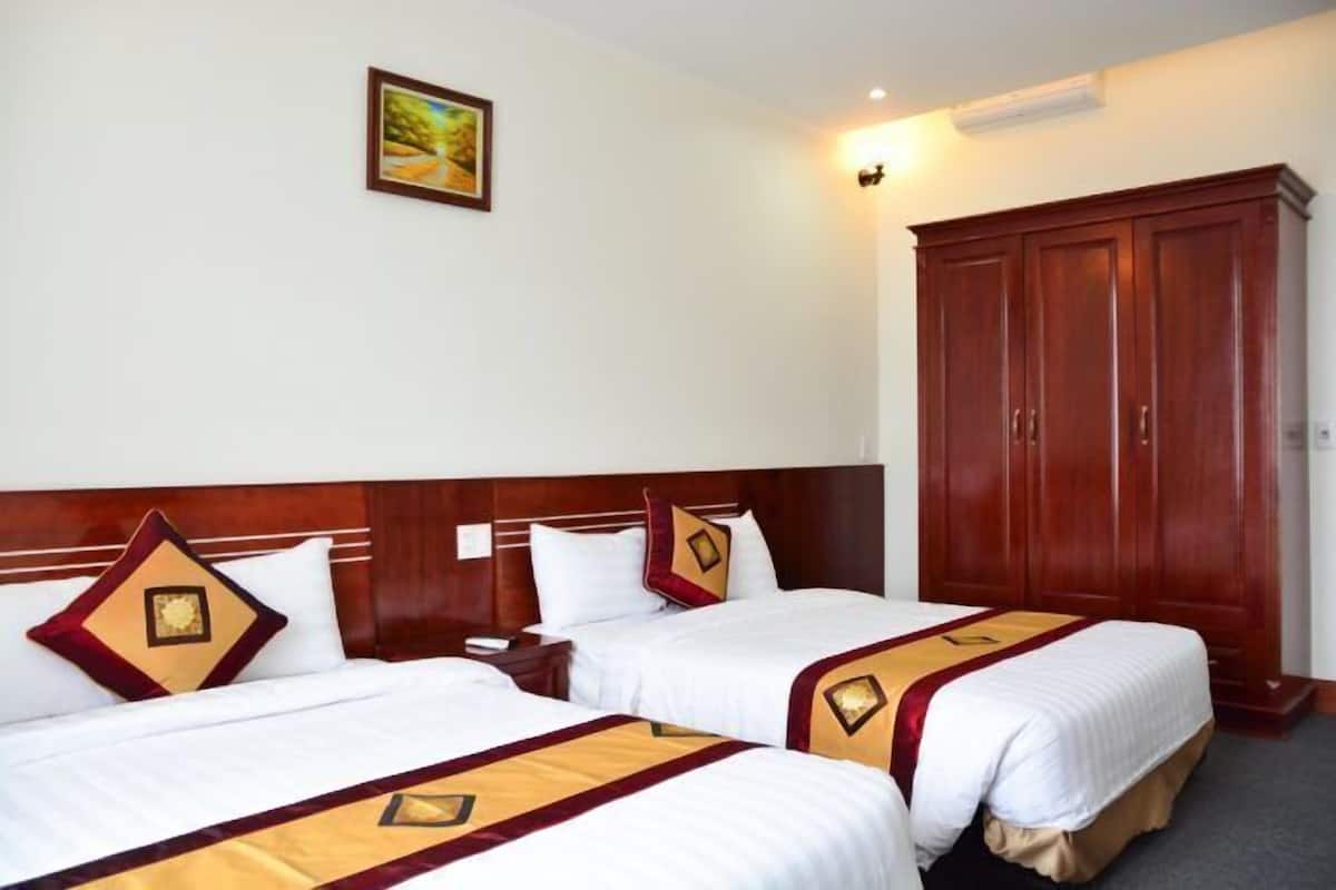 A hotel room with two beds, a wooden wardrobe, and a painting on the wall.