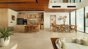 Een moderne keuken met houten kasten, een eethoek met een tafel en stoelen, en een groot raam met uitzicht op een zwembad.