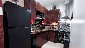 A compact kitchen with a black refrigerator, wooden cabinets, a microwave, a toaster, and a sink.