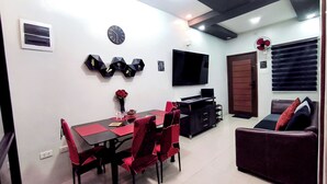 A modern living room with a sofa, a dining table with chairs, a flat-screen TV, and decorative wall art.