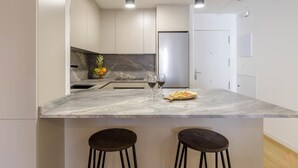 Una cocina moderna con encimera de mármol, dos taburetes y un frutero.