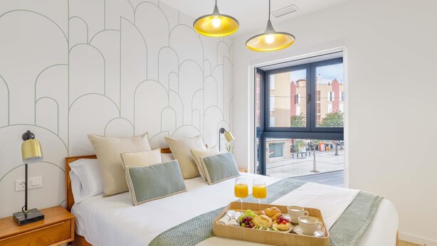 Habitación de hotel moderna con una cama grande, una bandeja de desayuno y vistas de la ciudad a través de la ventana.