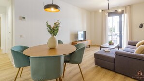 Una sala de estar moderna con una mesa de comedor redonda de madera, sillas color turquesa, un sofá gris y un televisor sobre un mueble de madera.
