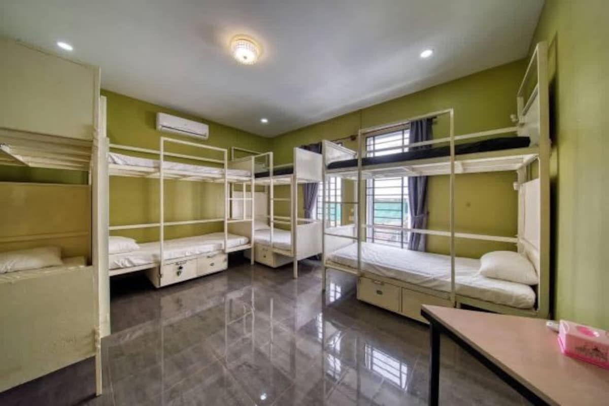 Une chambre de dortoir avec des lits superposés, une petite table et une fenêtre avec des rideaux.