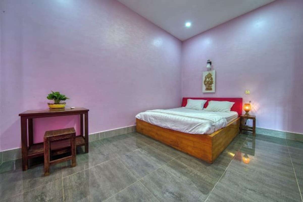Une chambre à coucher avec un lit, une table de chevet, une table avec une chaise et une petite plante.