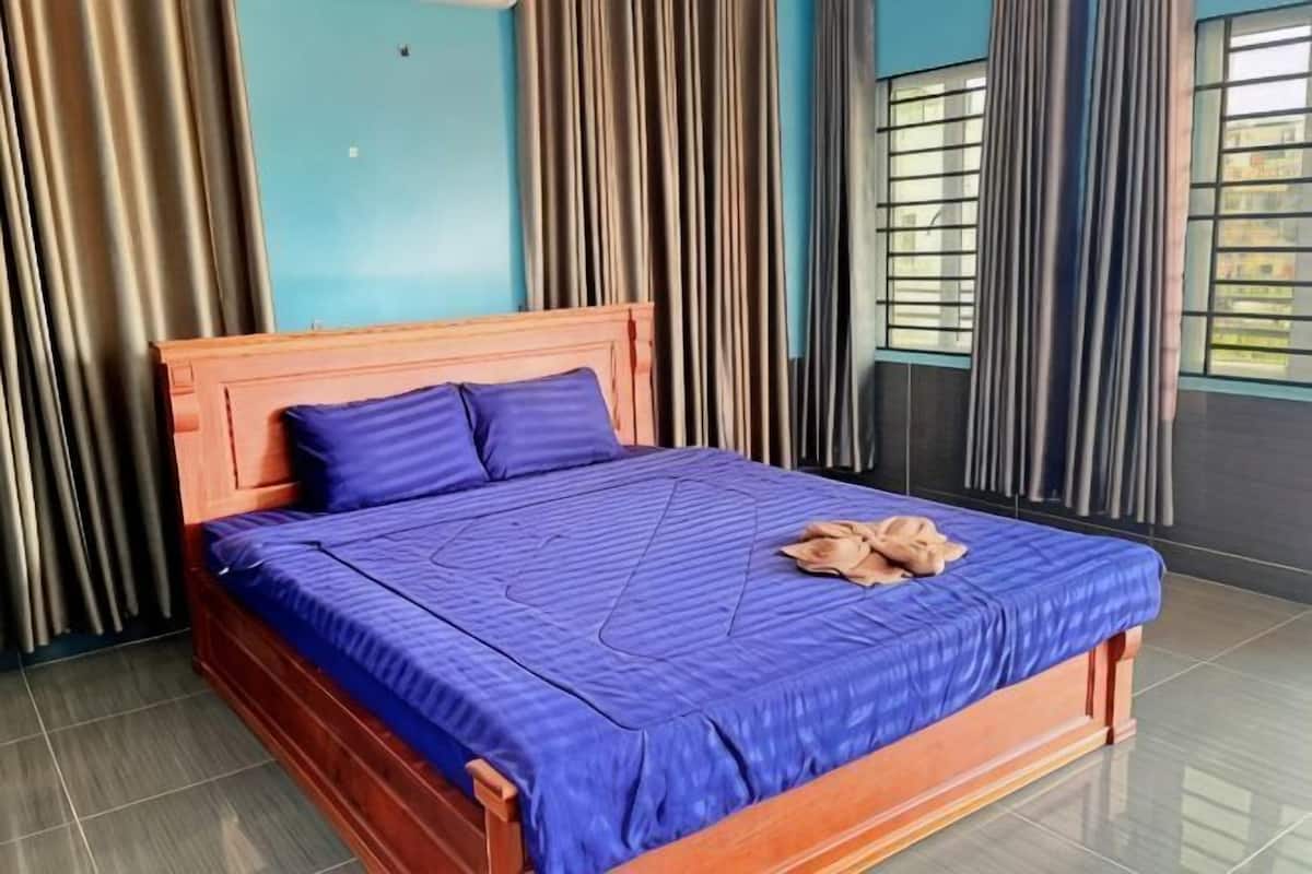 Ein ordentlich bezogenes Bett mit blauer Bettdecke und Kissen, einem Holzkopfstück und einem Handtuch auf dem Bett.