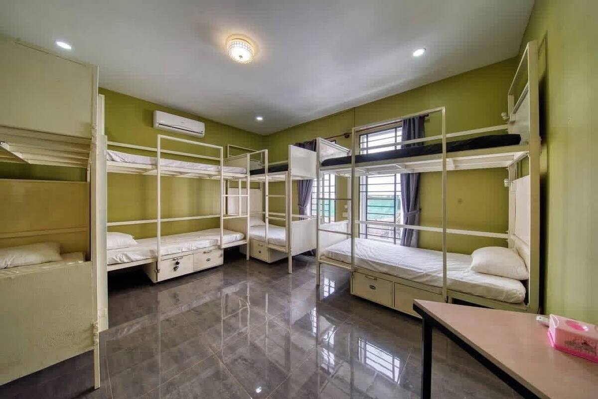 Ein Schlafsaalzimmer mit Etagenbetten, einem kleinen Tisch und einem Fenster mit Vorhängen.