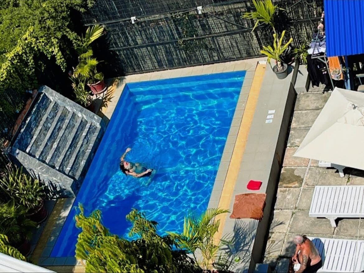 Une piscine où une personne nage, entourée de plantes en pot et de mobilier d’extérieur.