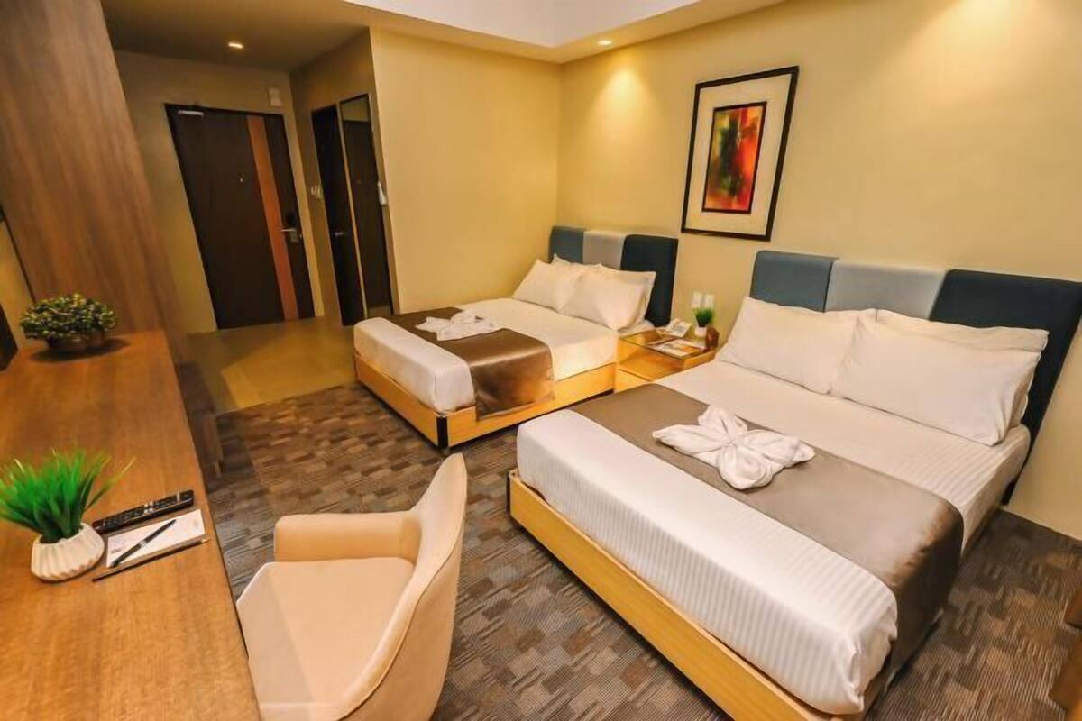 A hotel room with two beds, a desk with a chair, and a small plant.