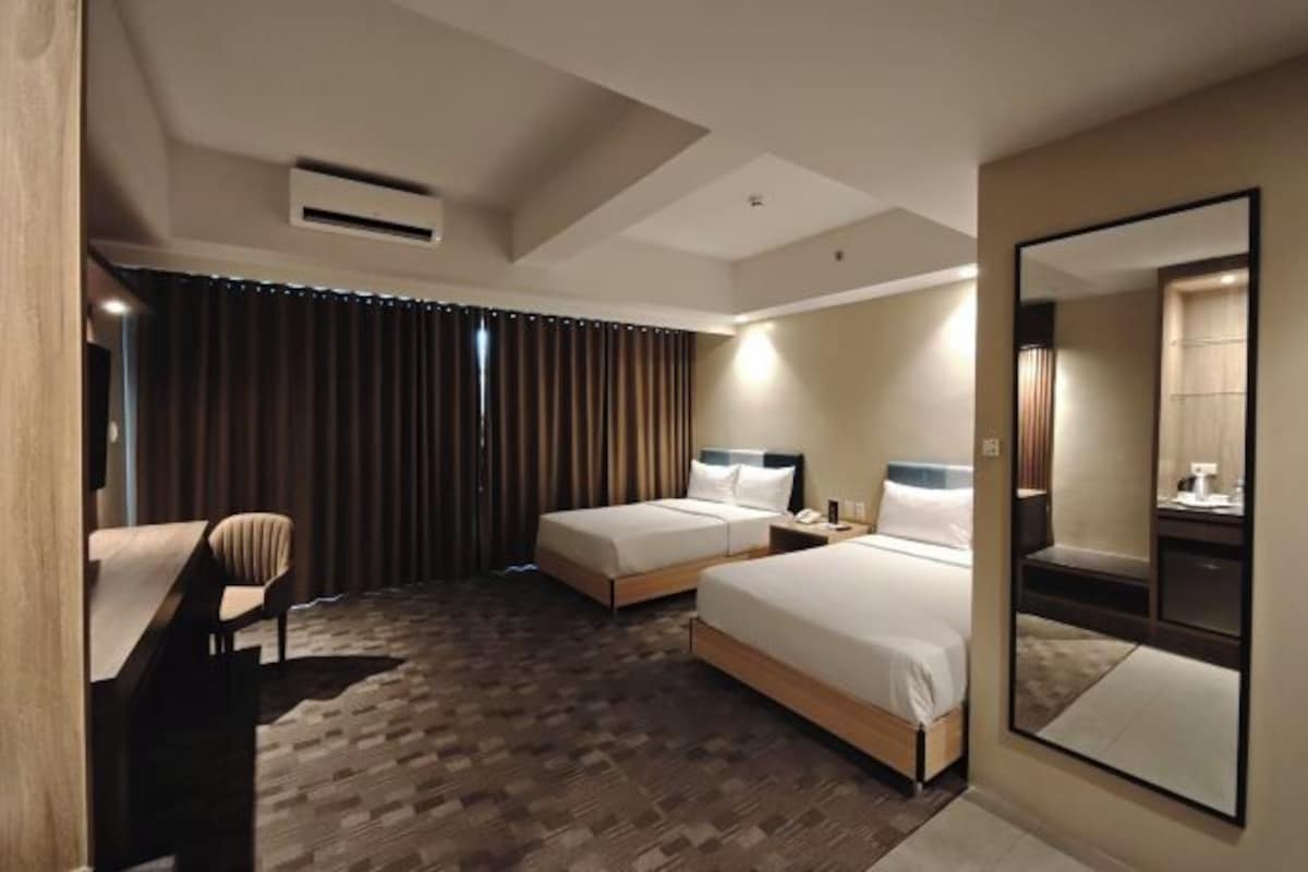 A hotel room with two beds, a desk, a chair, a mirror, and a window with curtains.