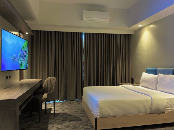 A hotel room with a bed, a desk with a TV, a chair, and a window with curtains. - The Tribute Hotel (Quezon City)