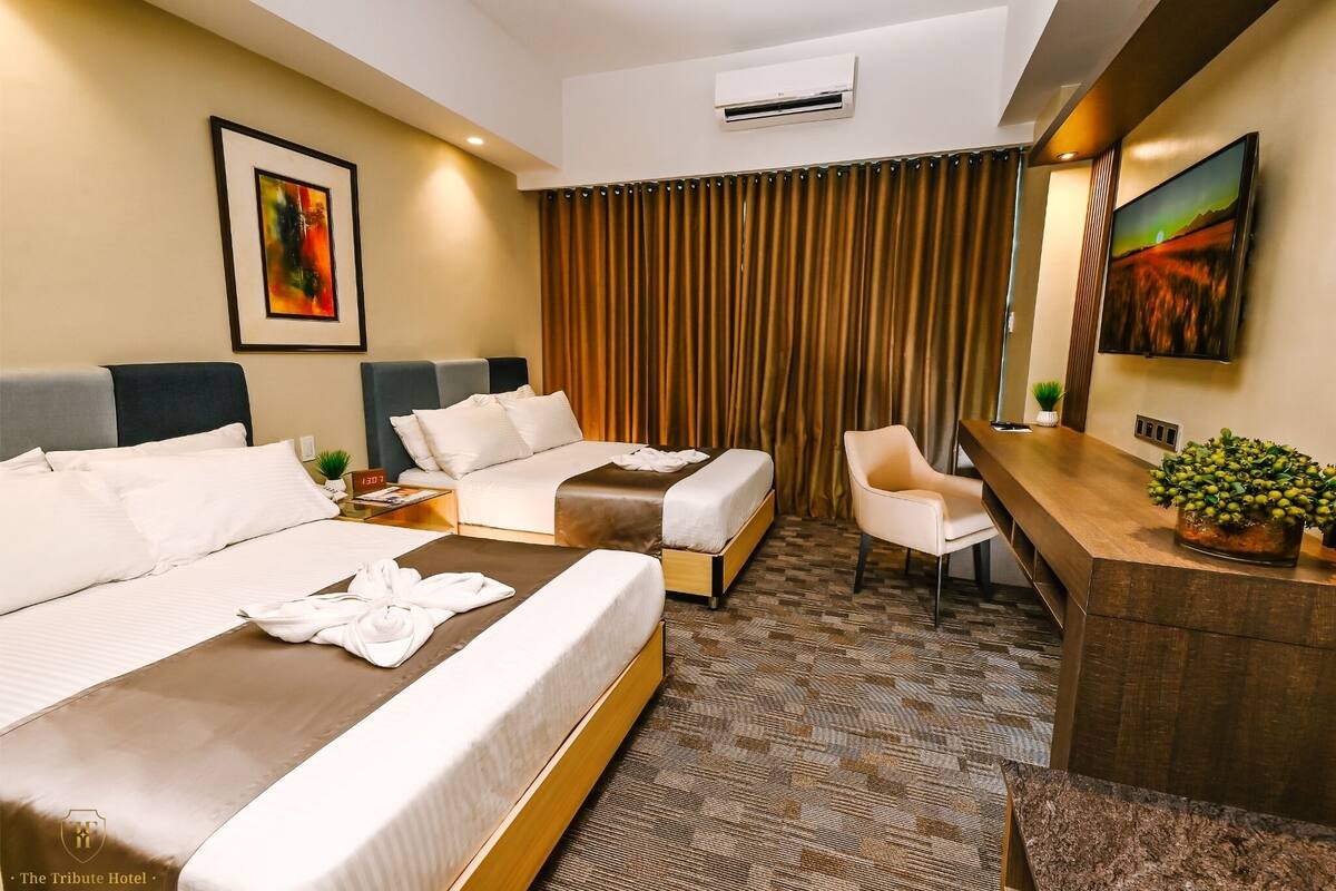 A hotel room with two beds, a desk, a chair, a TV, and a curtain.