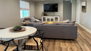 Un salon moderne avec un canapé gris, une table à manger blanche et un téléviseur fixé au mur.