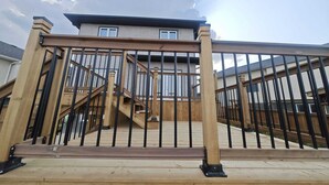 Um deck de madeira com guarda-corpo de metal que leva a uma casa com chaminé e janelas.