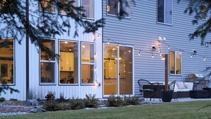 Una casa moderna con amplios ventanales, un patio con mobiliario exterior y un césped bien cuidado.