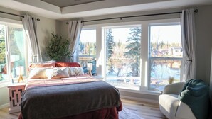 Un dormitorio con una cama grande, una silla y vistas a un lago y árboles.