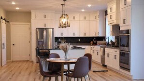 Una cocina moderna con armarios blancos, electrodomésticos de acero inoxidable y un comedor con una mesa redonda y sillas.