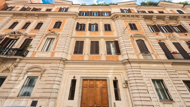 A multi-story building with classical architecture, featuring a central entrance with a large wooden door, multiple windows with shutters, and balconies. - Vittorio Emanuele | Luxe Flat (Roma)