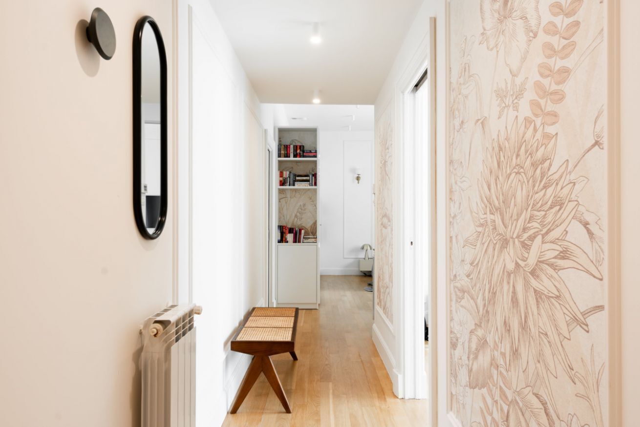 A hallway with a radiator, a mirror, a small wooden stool, and a bookshelf.
