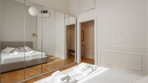 A modern hotel room with a large mirror, a bed with white linens, and a wooden floor. - Vittorio Emanuele | Luxe Flat (Roma)