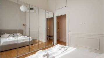 A modern hotel room with a large mirror, a bed with white linens, and a wooden floor.