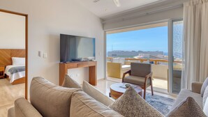 Une chambre d’hôtel moderne dotée d’un grand canapé, d’une télévision à écran plat, d’un coin repas et d’un balcon offrant une vue sur la ville.