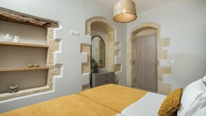Une chambre à coucher avec un lit, une étagère en bois, un miroir et une porte ornée d’arcs en pierre.