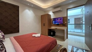 A modern hotel room with a large bed, a TV, a wooden wardrobe, and a view of the outside. - Blue Moon Residency Sector 53 Gurgaon (Gurugram)