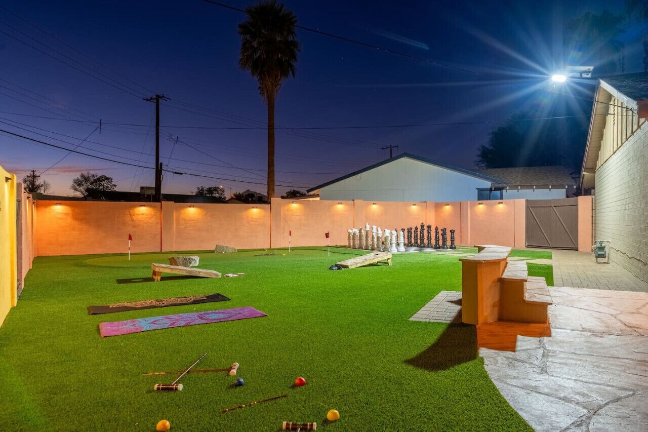 A well-lit backyard with artificial grass, a wooden bench, and a small table.