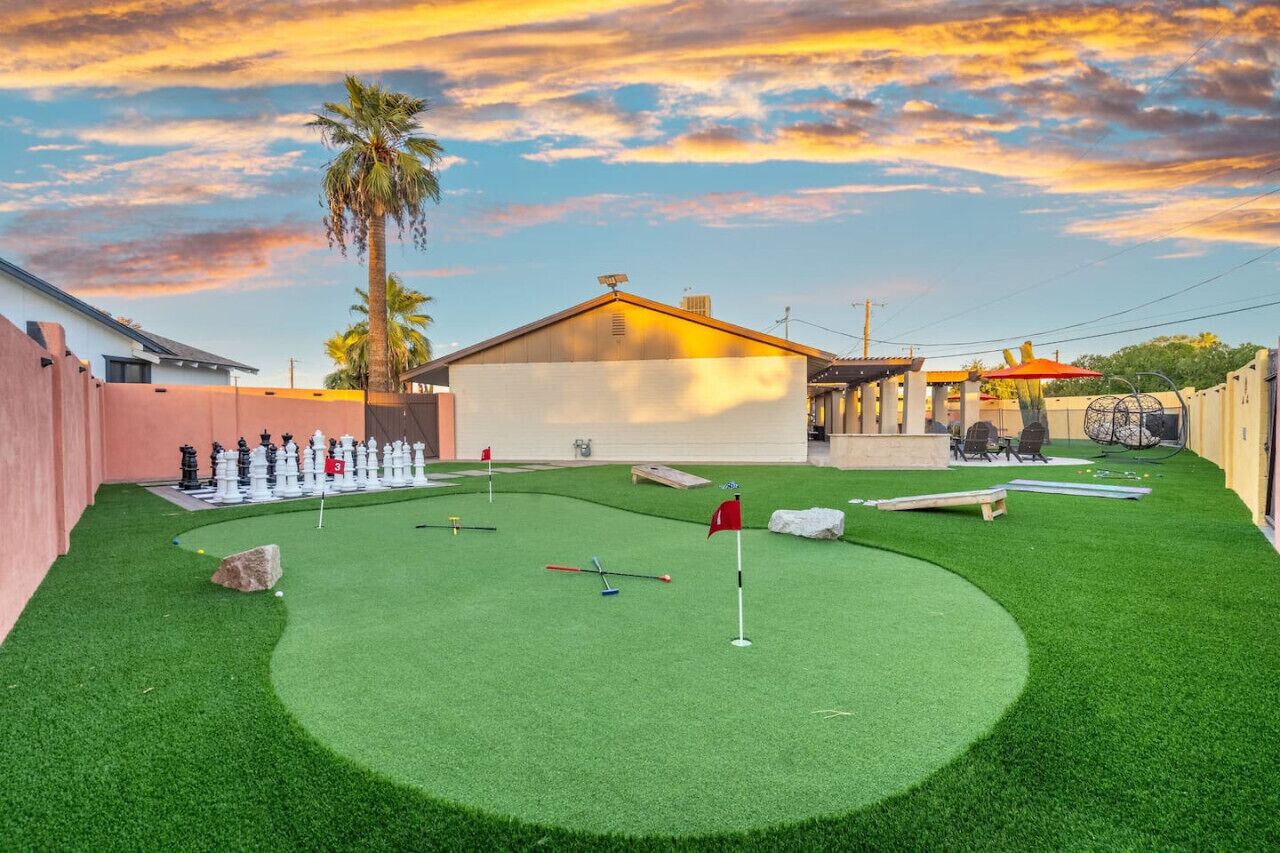 A golf course with a putting green, a white building, and palm trees.