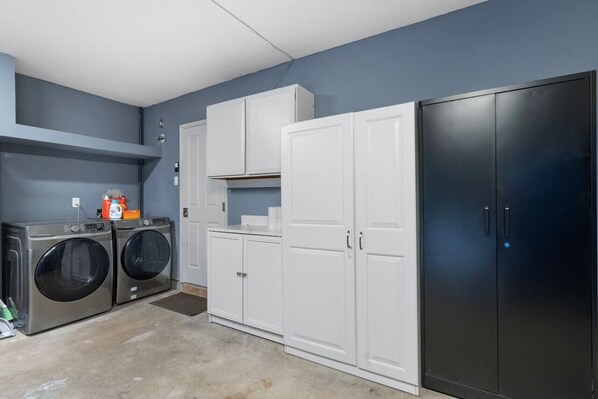 A laundry room with two front-loading washers, a dryer, and white cabinets.