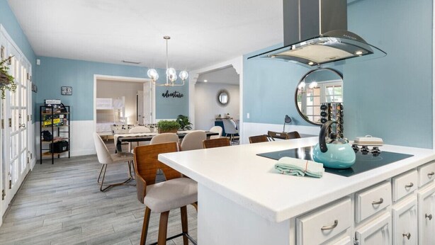 Een moderne keuken met een centraal eiland, een eethoek met stoelen, en een zichtbaar aanrecht.