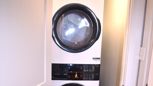 A laundry room with two stacked front-loading washing machines and a black hexagonal tile floor. - 3-bedroom in Mid City, walking distance to LSU lakes, Garden District (Baton Rouge)