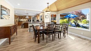 A spacious kitchen with wooden cabinets, a dining area with a large table and chairs, and a view of a swimming pool through large windows.