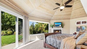 A bedroom with a large bed, a ceiling fan, a fireplace, and a TV.