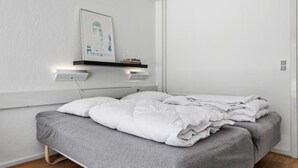 Una habitación de hotel moderna con una cama, una mesita de noche, un estante en la pared con libros y un cuadro enmarcado.
