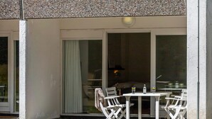 Un área de estar al aire libre con una mesa y sillas, una puerta corrediza de vidrio y vistas a un edificio con fachada de piedra.