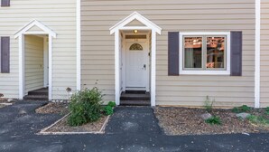 A two-story house with a front door, a small porch, and a window with shutters.