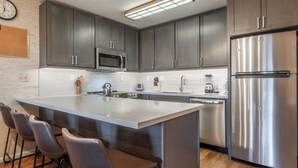 A modern kitchen with dark cabinets, stainless steel appliances, a large island with bar stools, and a clock on the wall.
