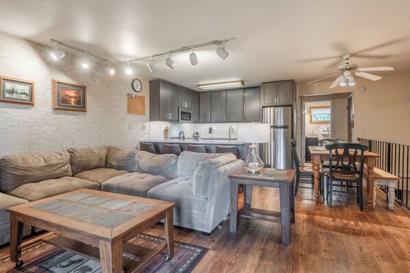 A modern living room with a sectional sofa, a coffee table, and a dining area with a table and chairs. - New Pet-Friendly Cozy Condo w/ Relaxing Spa 601 (Mammoth Lakes)