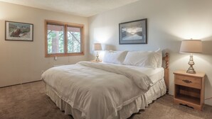 A bedroom with a large bed, two bedside lamps, a nightstand, and two framed pictures on the wall.