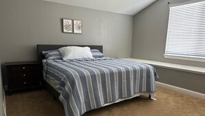 A bedroom with a bed, a nightstand, a window with blinds, and two wall-mounted pictures. - Spacious 5-bedroom house in delightful Elk Grove with AC, WiFi,fitness equipment (elk grove)
