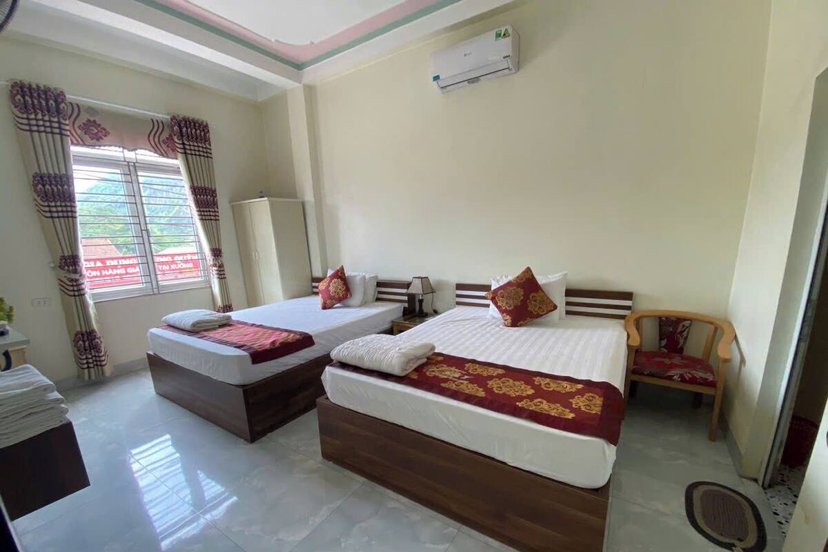 A hotel room with two beds, a wooden headboard, a small wooden chair, and a window with curtains.