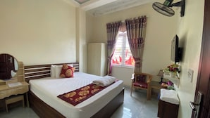 A hotel room with a large bed, a desk with a mirror, a chair, a wardrobe, and a small table with a lamp and flowers. - Sky Hotel Moc Chau - by BAY LUXURY (Moc Son)