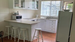 A kitchen with white cabinets, a microwave, a sink, and a refrigerator. There are three white stools and a colorful rug on the floor.
