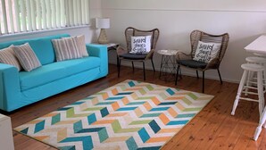A room with a blue sofa, two wicker chairs, a small table, and a patterned rug.