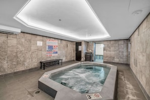 Un'area benessere con vasca idromassaggio, pareti in marmo e una panca.