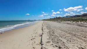 Une vaste plage de sable fin, bordée par l’océan, avec des vagues, un ciel dégagé et des propriétés situées en bord de mer.