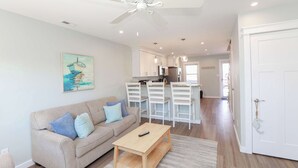 A modern living room with a sofa, a coffee table, and a ceiling fan. - Sojourn's Sea Views with Balcony Sleeps 4 (Virginia Beach)