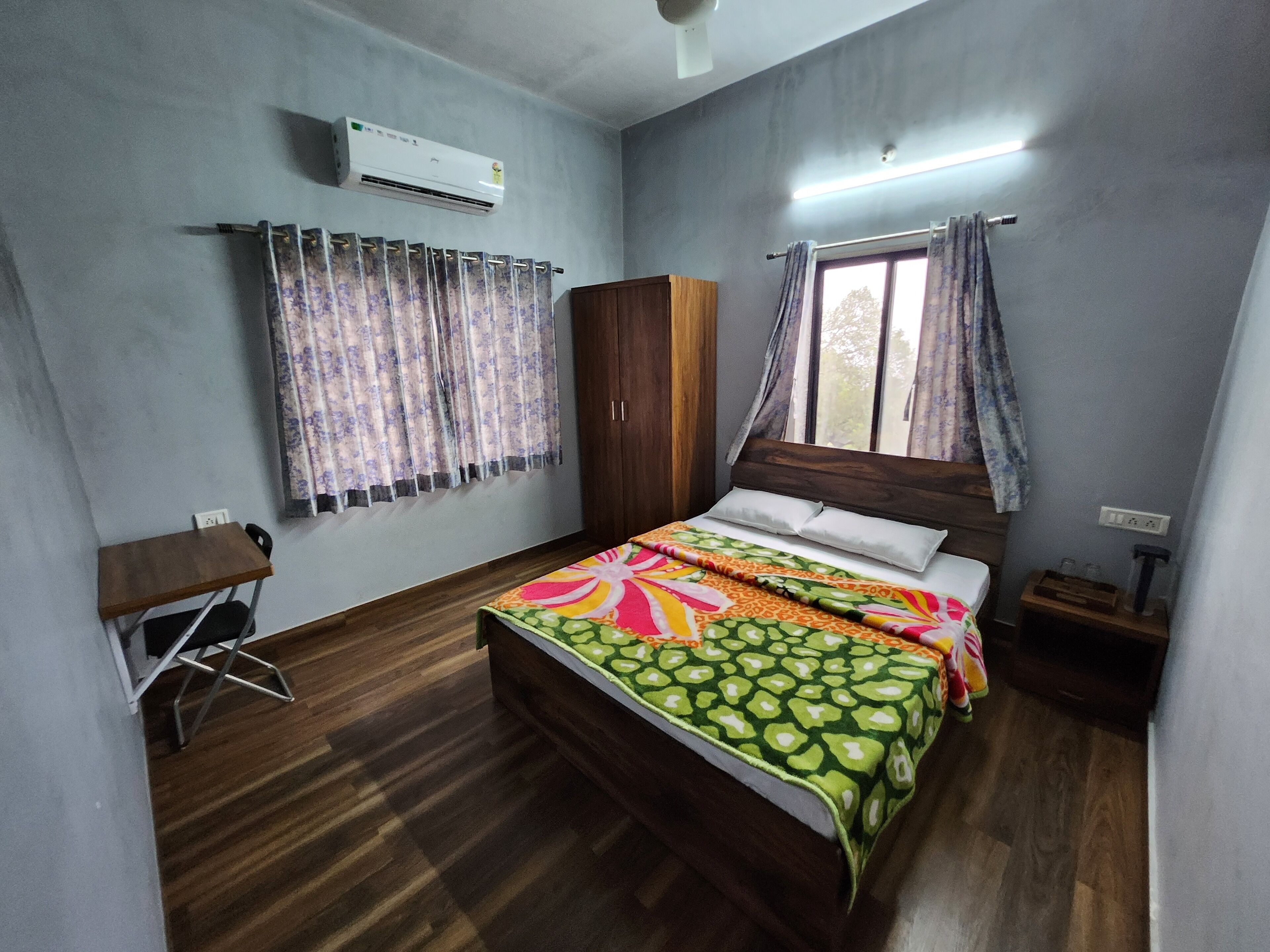 A bedroom with a wooden bed, a desk, a wardrobe, and an air conditioning unit.